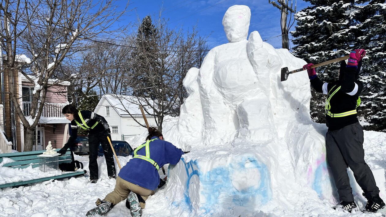 Des gens s'affairent à sculpter un bloc de neige où une forme humain prends tranquillement forme.