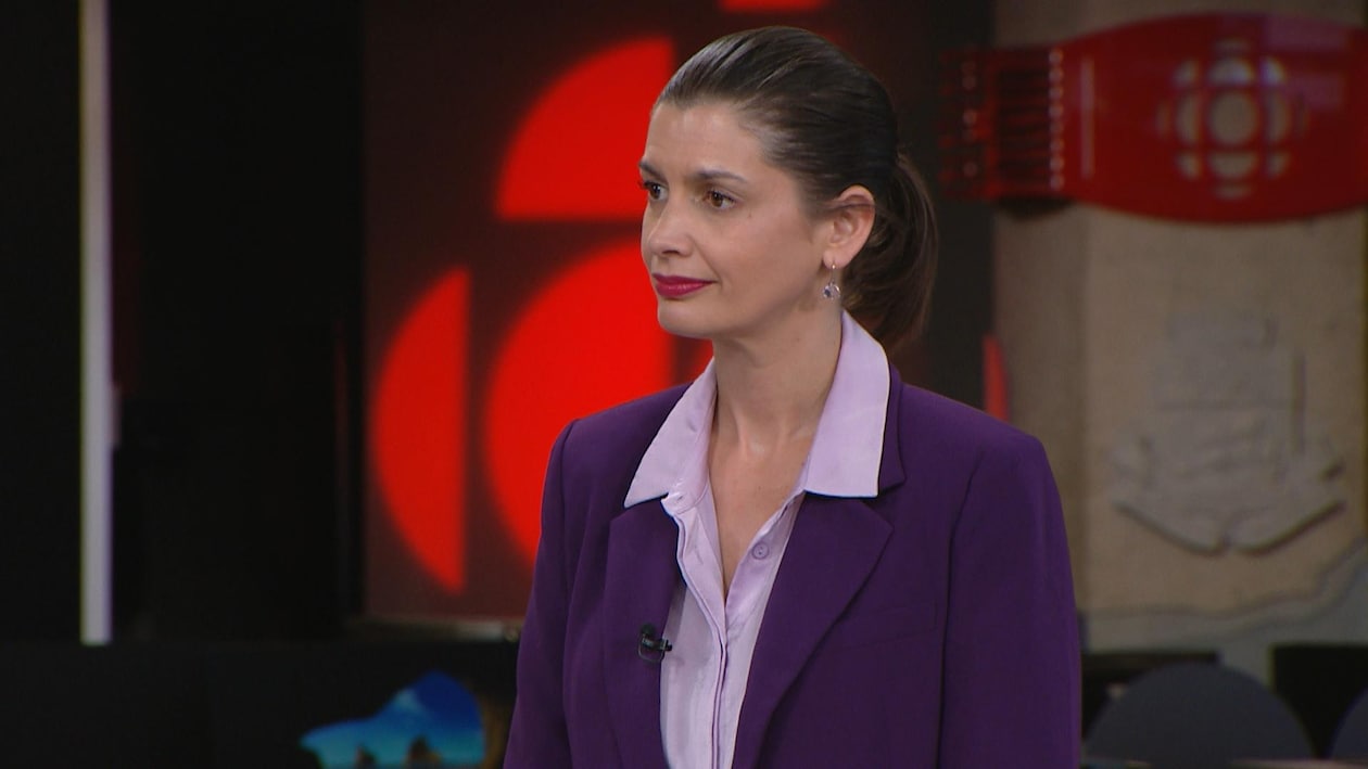 Geneviève Guilbault porte une chemise lilas et un veston mauve sur un plateau télé. 