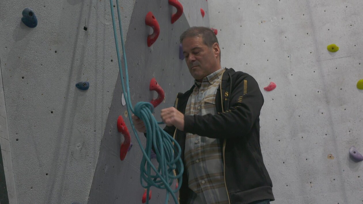 Un homme vérifie la solidité de câbles au pied d'un mur d'escalade. 