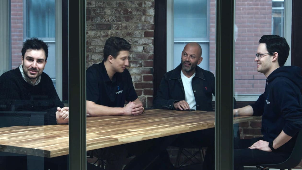 Quatre hommes parlent autour d'une table en bois.