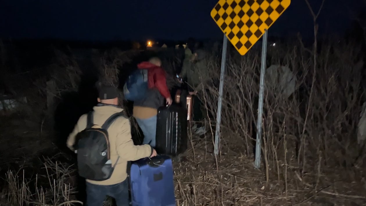 Des migrants illégaux traversent la frontière Canada-États-Unis la nuit avec leurs valises.