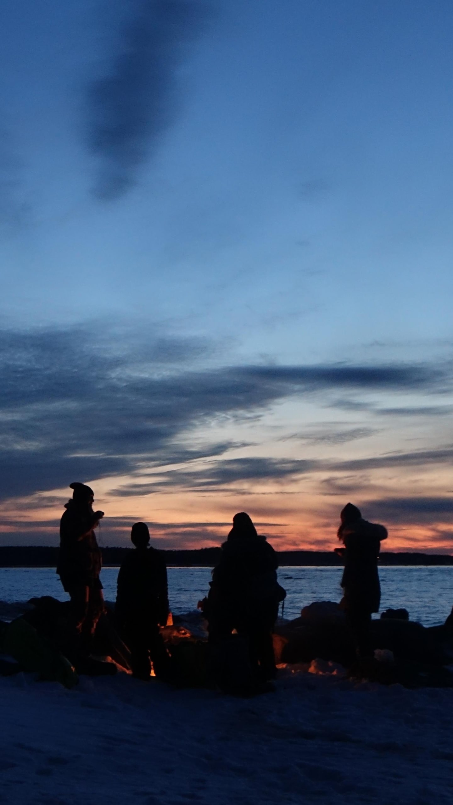 Des gens sont rassemblés autour du feu au coucher du soleil.