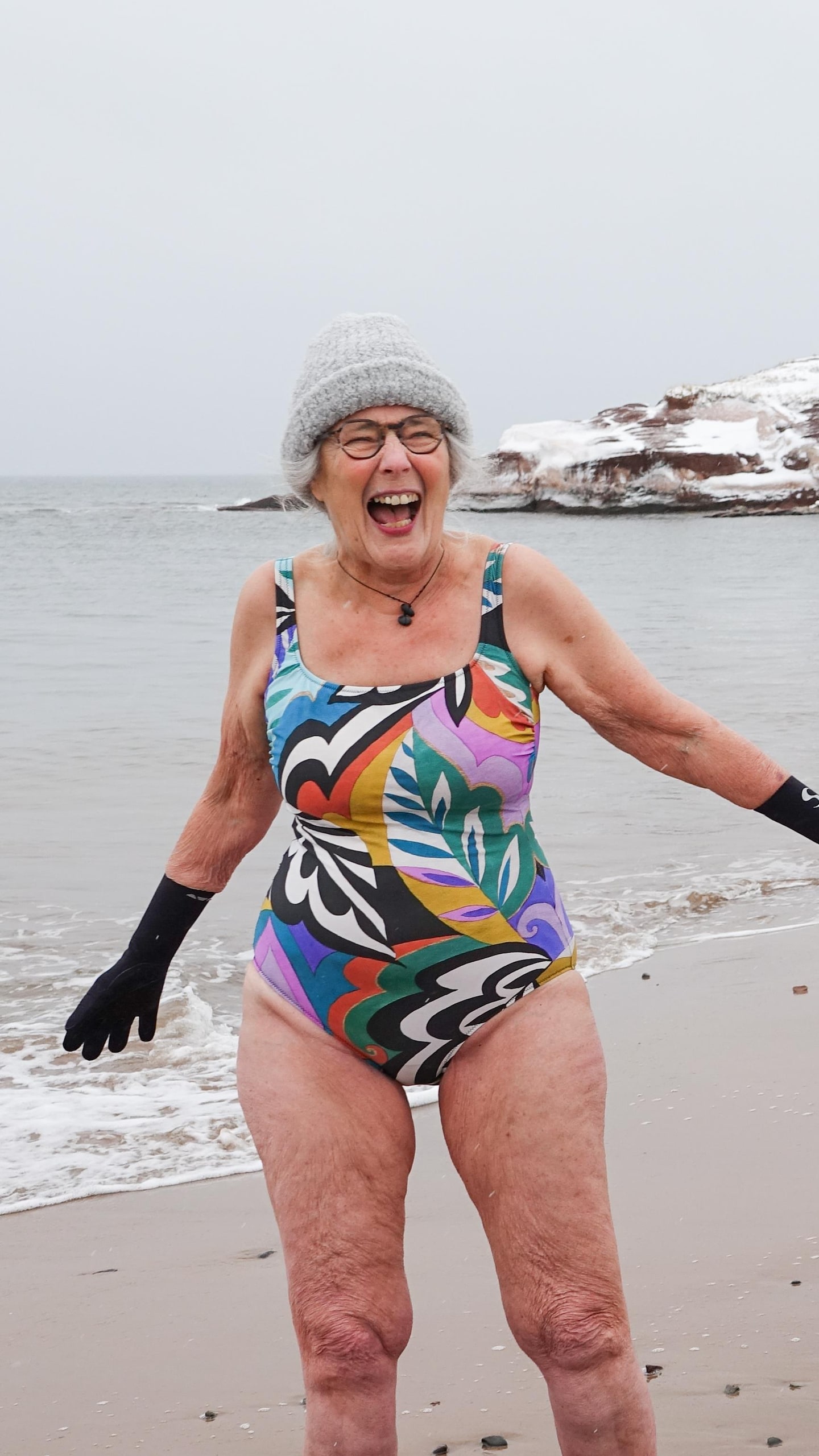 Nicole Grégoire et sa fille Pauline-Gervaise Grégoire se tiennent par la main en souriant, en maillot de bain, sur une plage enneigée des Îles-de-la-Madeleine.