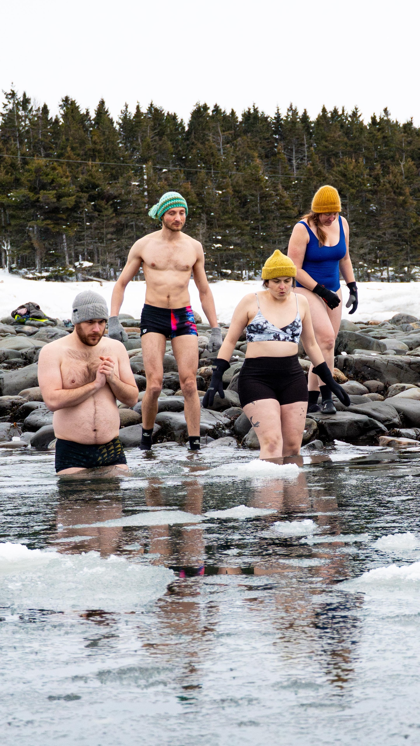 Des baigneurs et baigneuses entrent dans l’eau sur laquelle flottent des glaçons durant l’hiver.