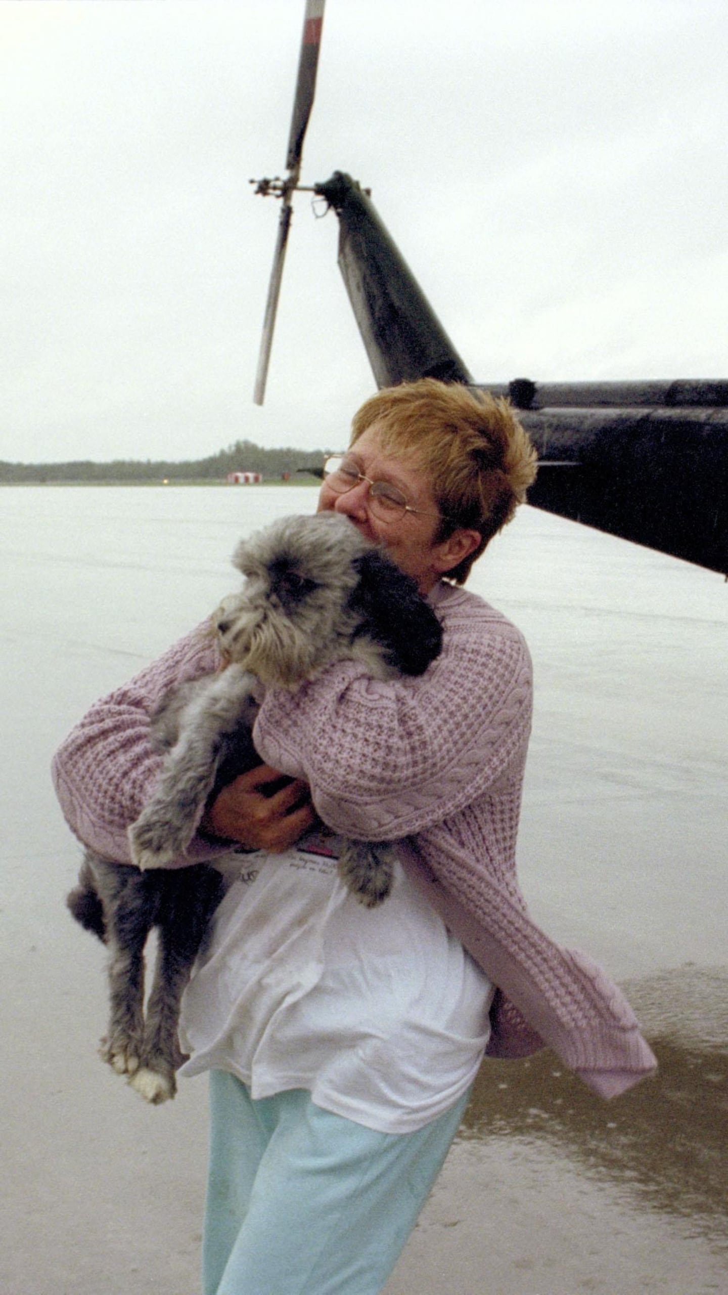 Une dame tient dans ses bras son chien devant un hélicoptère.