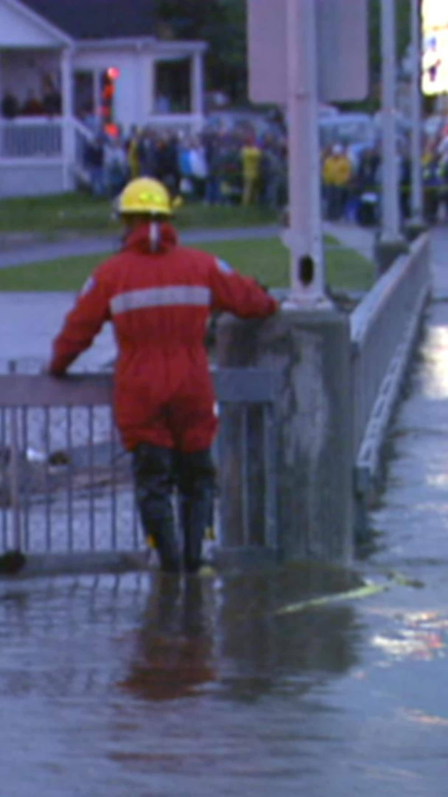 Un secouriste de dos devant un pont summergé par l'eau.