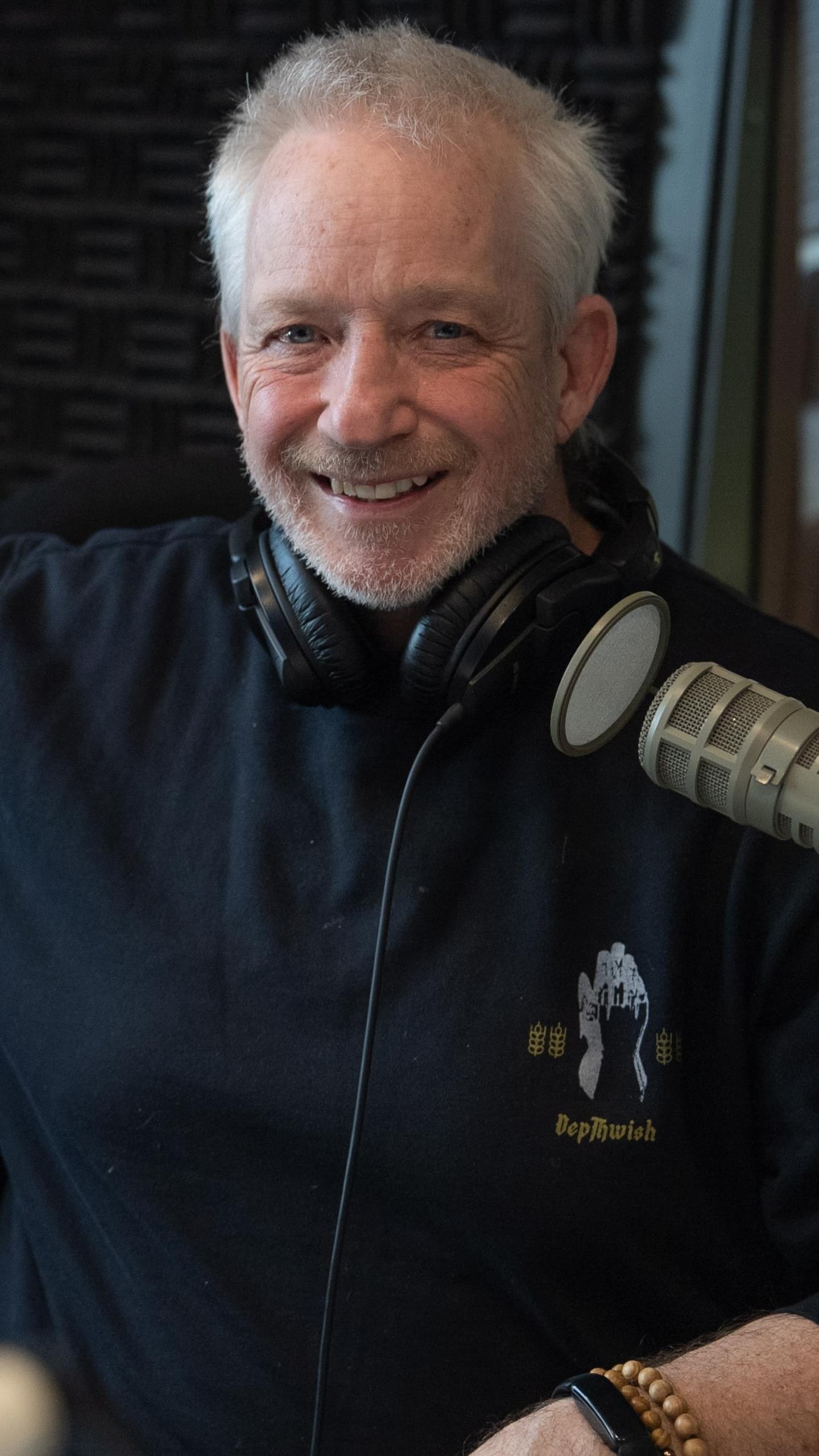 Jean Fontaine, un homme d'âge mûr souriant avec des lunettes, est assis dans un studio de radio devant un microphone professionnel.
