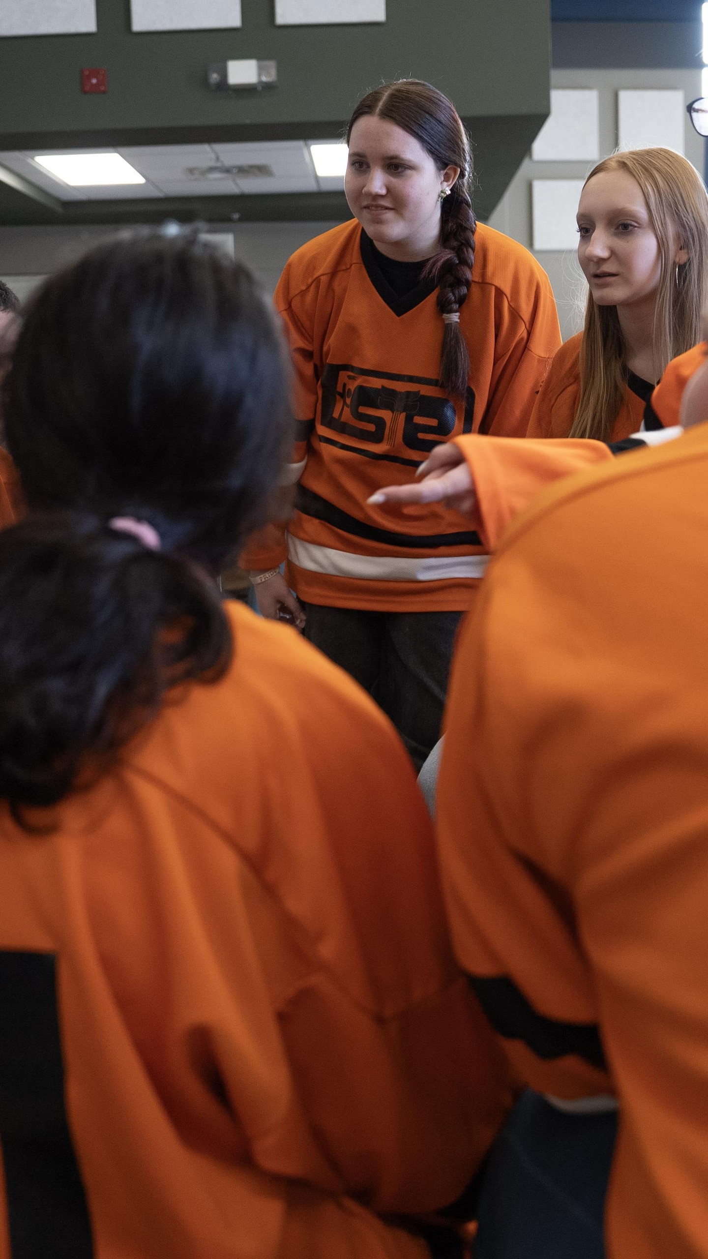Un groupe d'adolescents portant des chandails de hockey orange sont regroupés en cercle, discutant intensément de leur stratégie avant de monter sur scène.