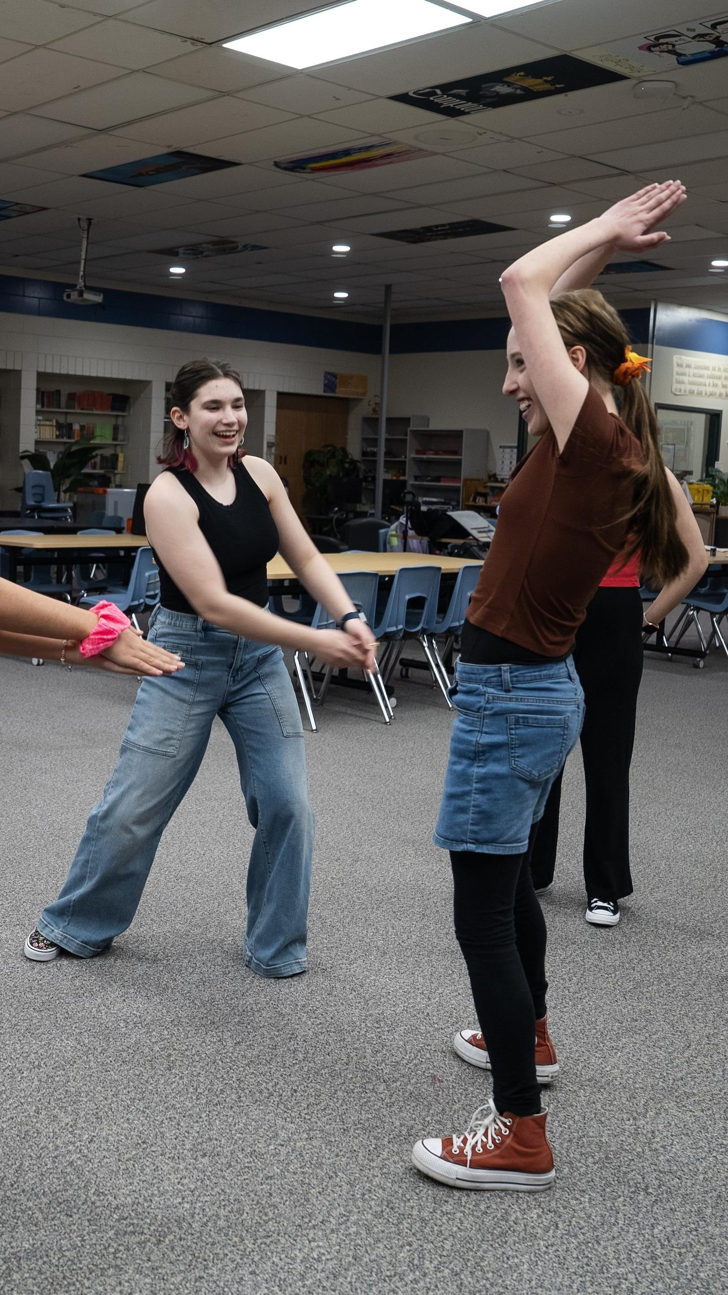 Un groupe d'élèves en vêtements civils participe à des exercices d'échauffement dynamique dans une bibliothèque, certains faisant des mouvements de bras et de jambes.