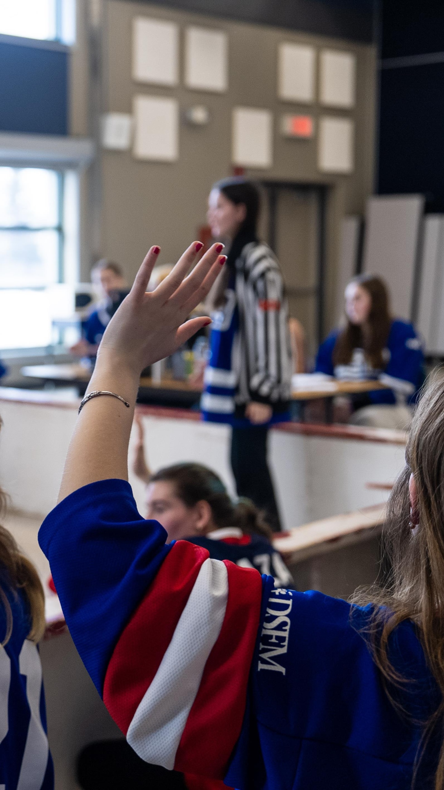 Plusieurs improvisateurs de dos, en chandails bleus et rouges, lèvent la main vers l'arbitre qui pointe une direction sur la scène.