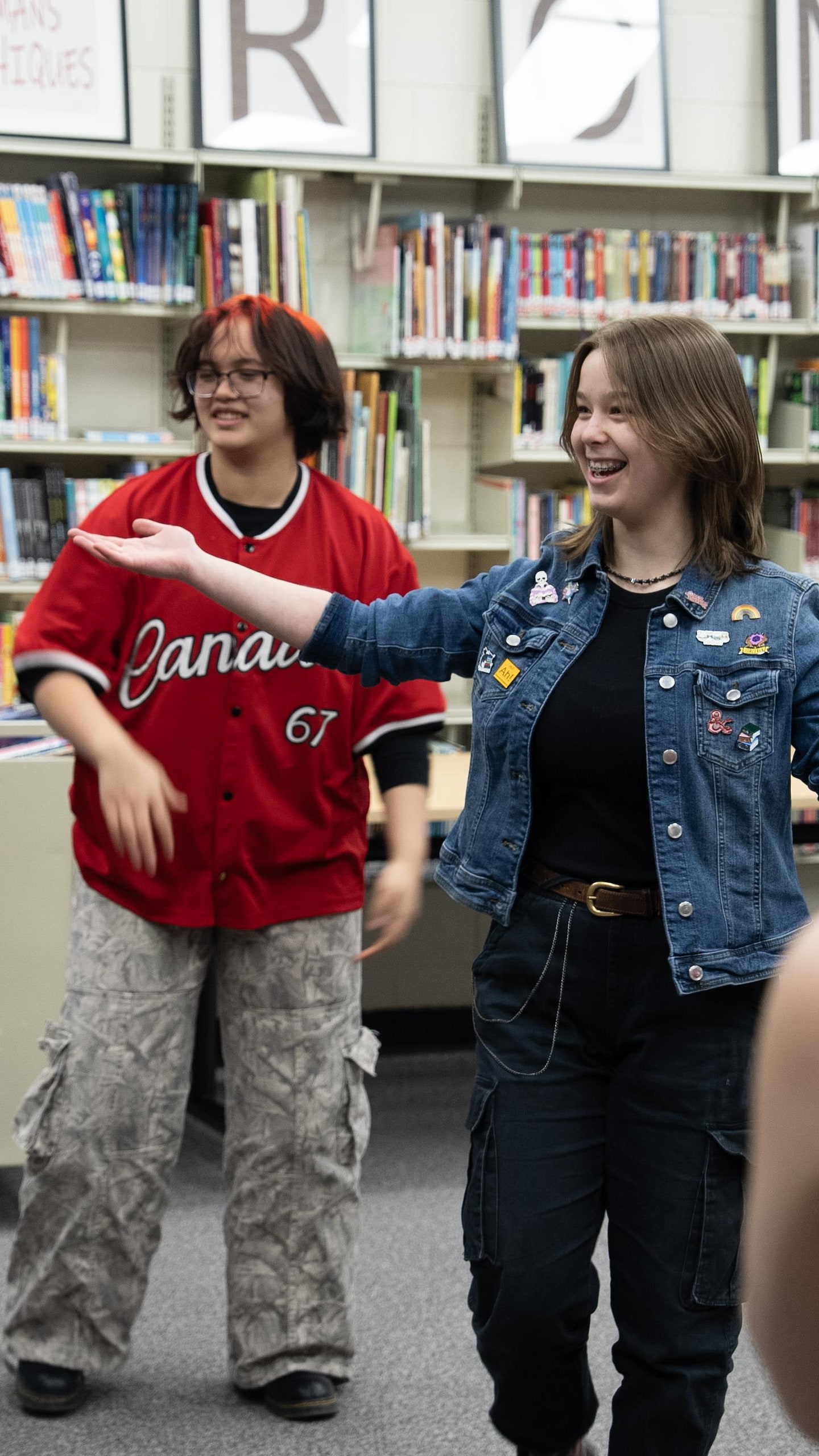 La jeune Rylee Cammaert, souriante, se tient au centre d'un cercle formé par ses camarades de classe dans une bibliothèque.