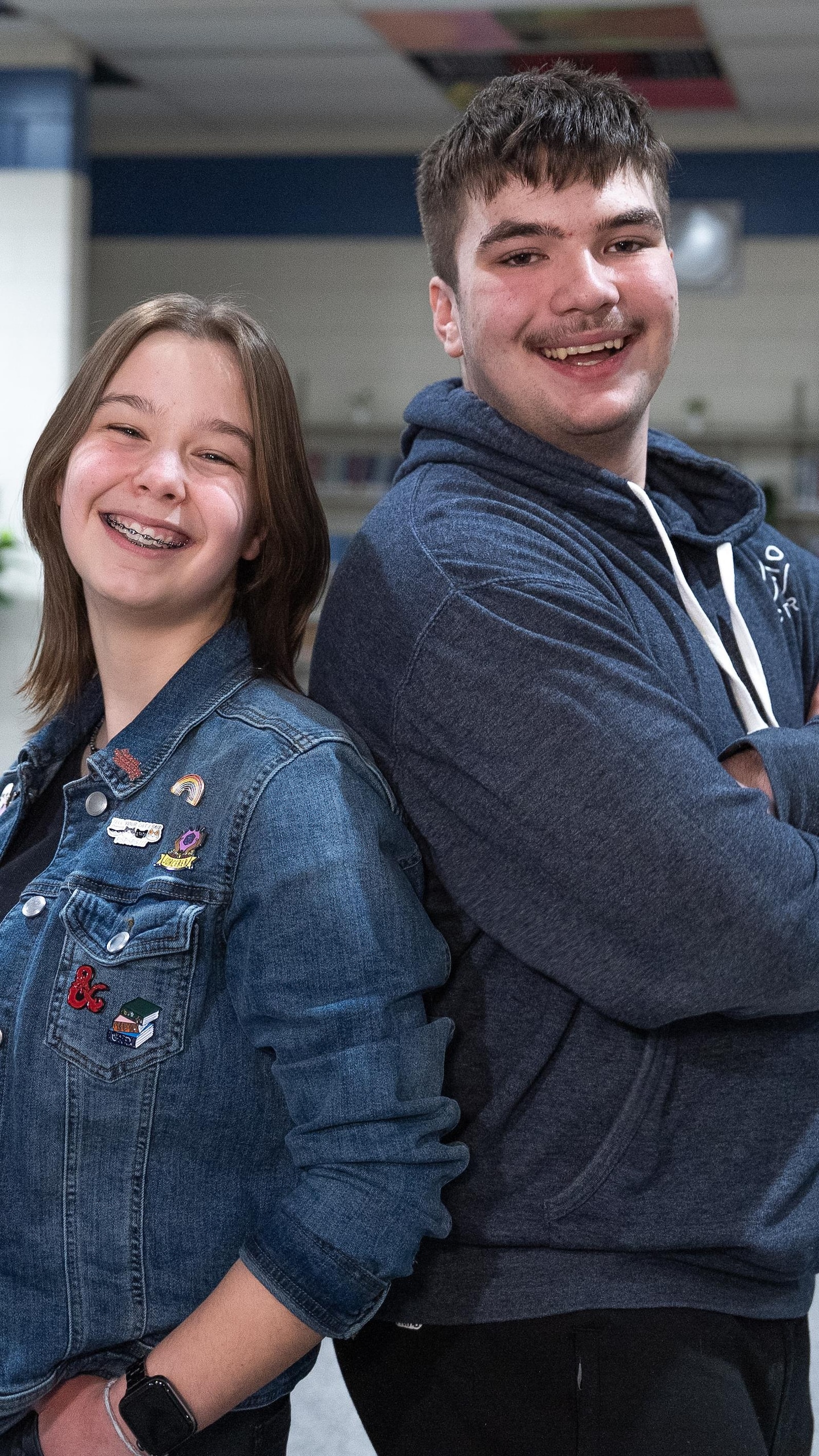 Les deux élèves, Rylee et Preston, posent dos à dos en souriant au milieu de la bibliothèque de leur école.