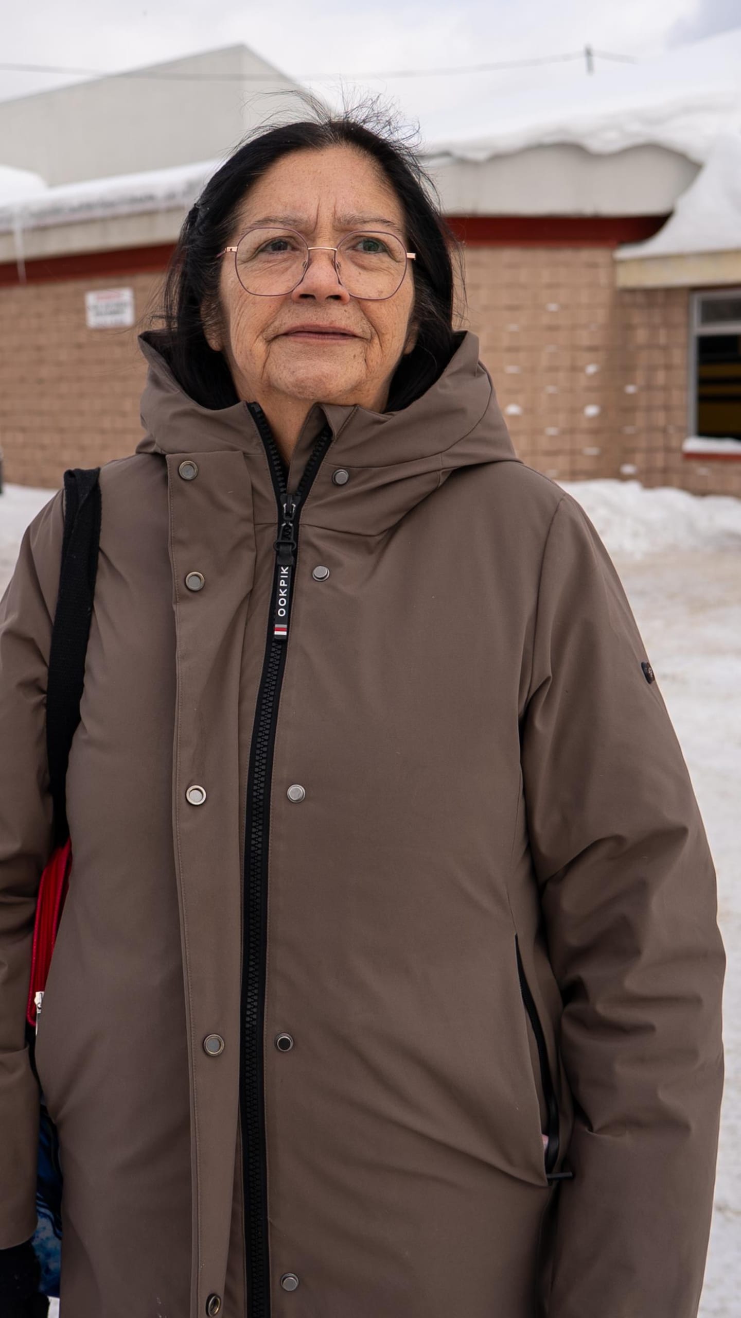 Frances Mowatt est debout devant l'école Migwan de Pikogan. Un autobus passe devant l'école.