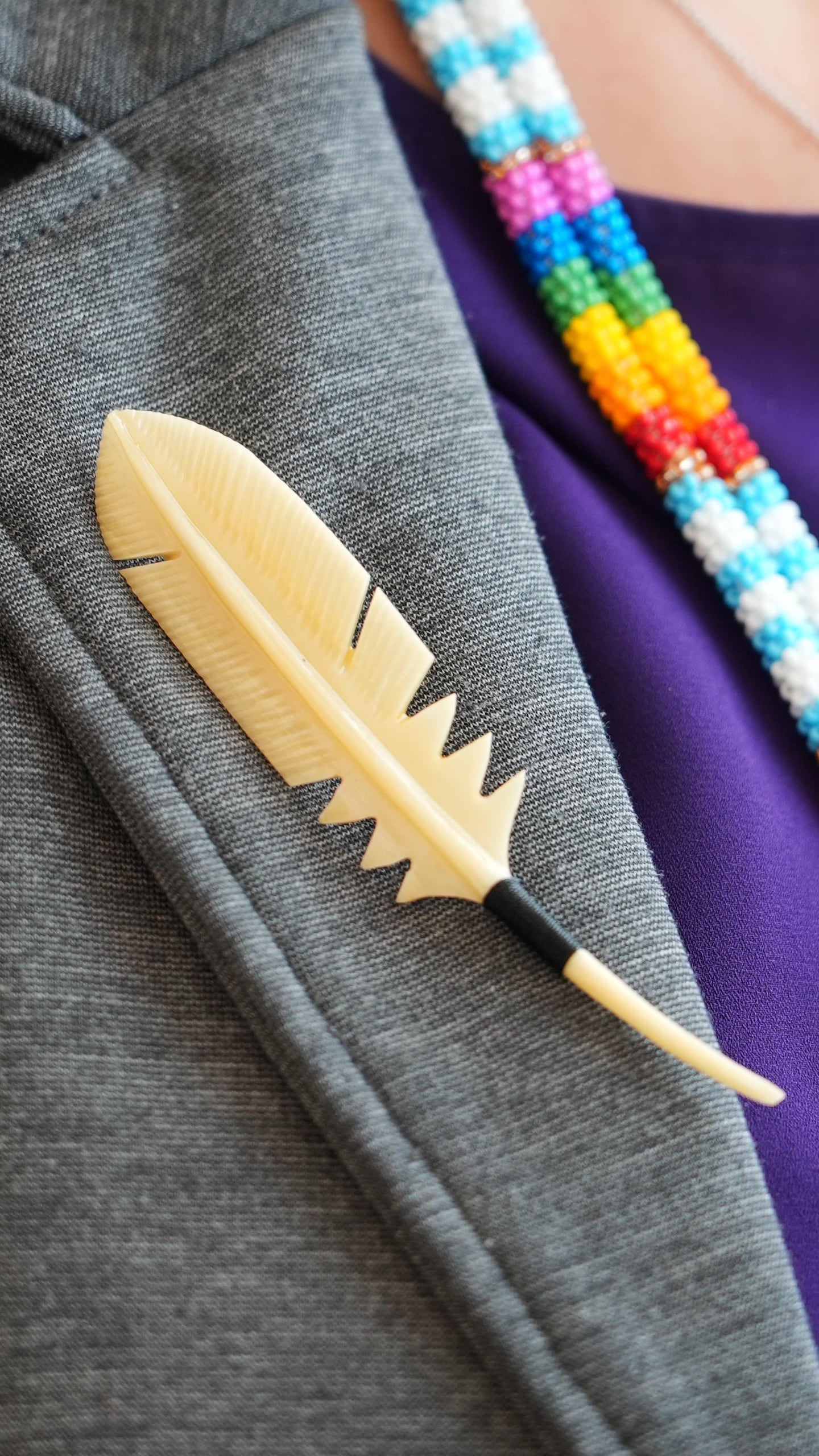 Un accessoire en forme de plume est positionné sur le veston de Suzy Basile.