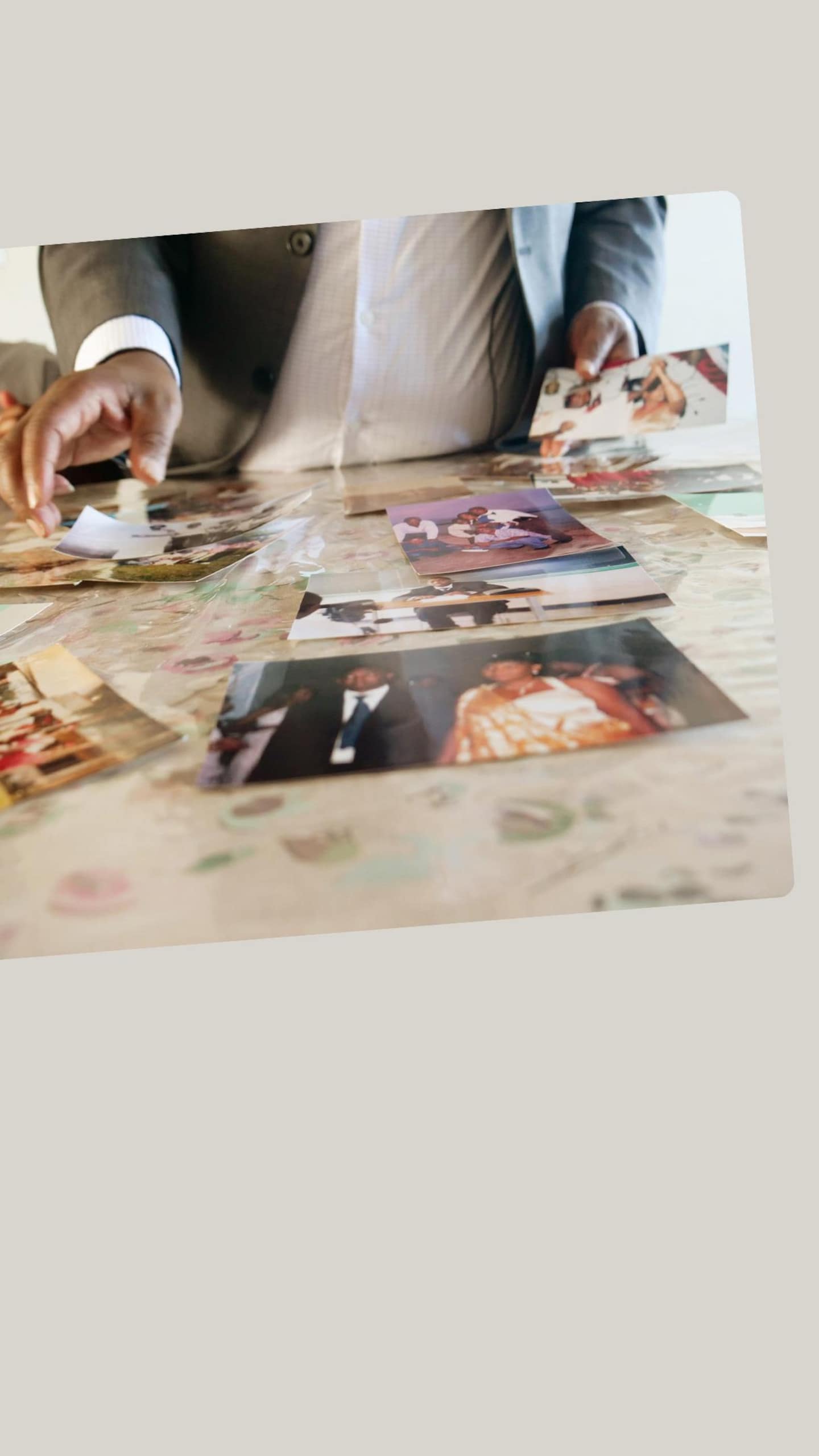 Vue en gros plan et en contre-plongée sur une table où sont éparpillées plusieurs photographies imprimées. Les mains d'un homme en costume gris manipulent et déplacent les photos sur la surface de la table.