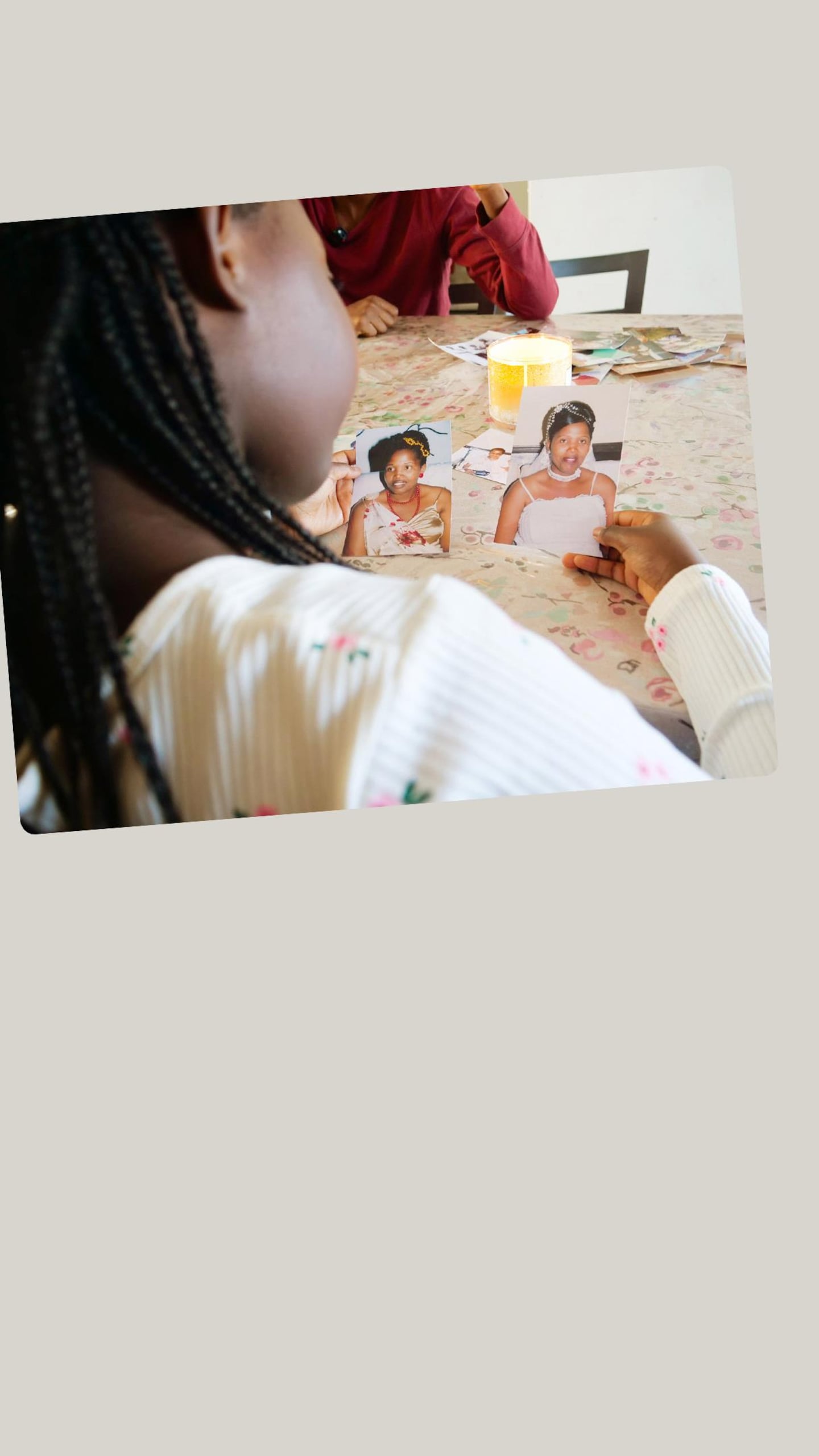 Vue par-dessus l'épaule d'une jeune fille observant deux petites photographies posées sur une table à côté d'une bougie allumée. Les photos montrent des portraits de fillettes en robes blanches.