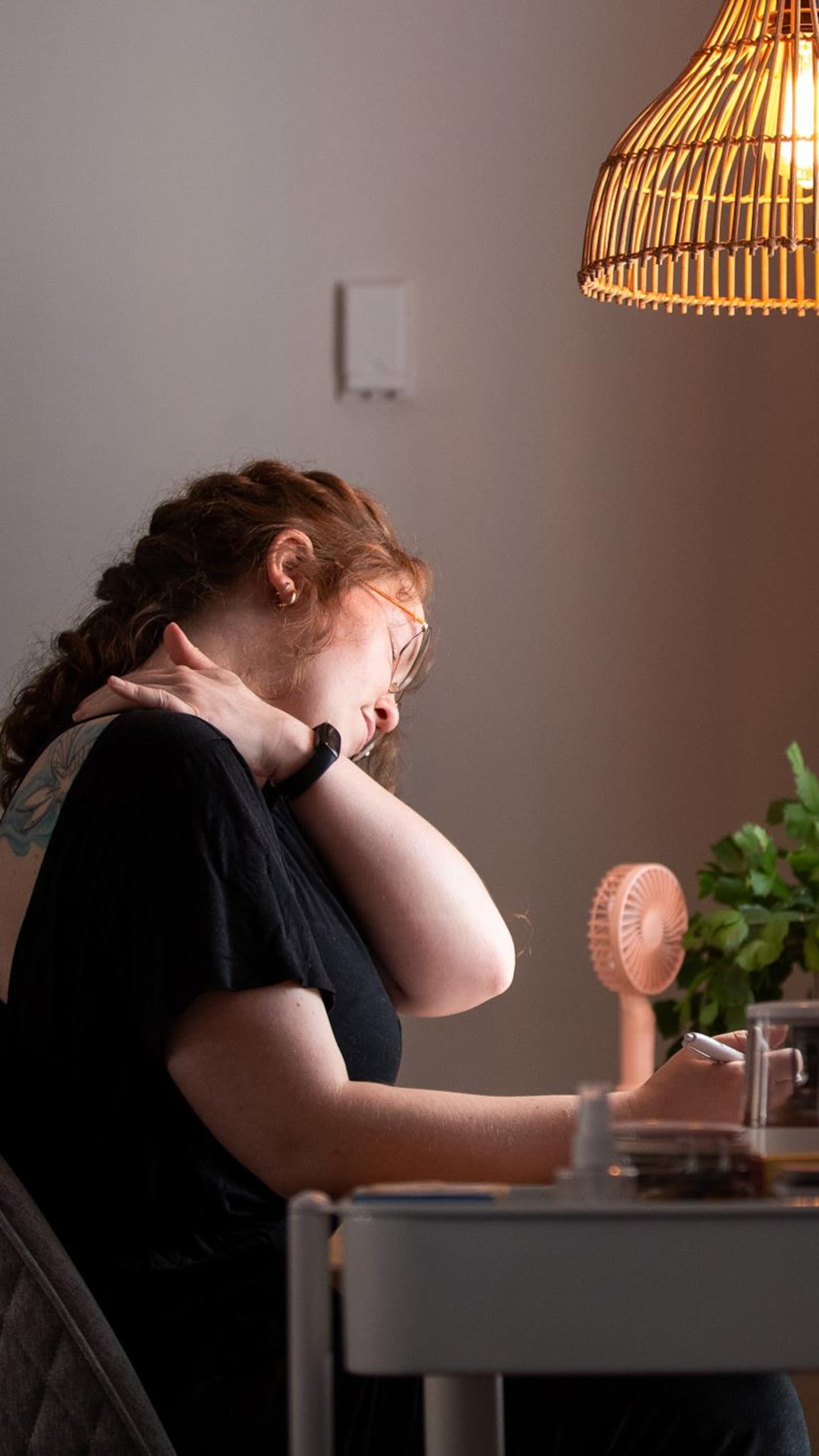 Une personne, assise à un bureau, se touche l'épaule.