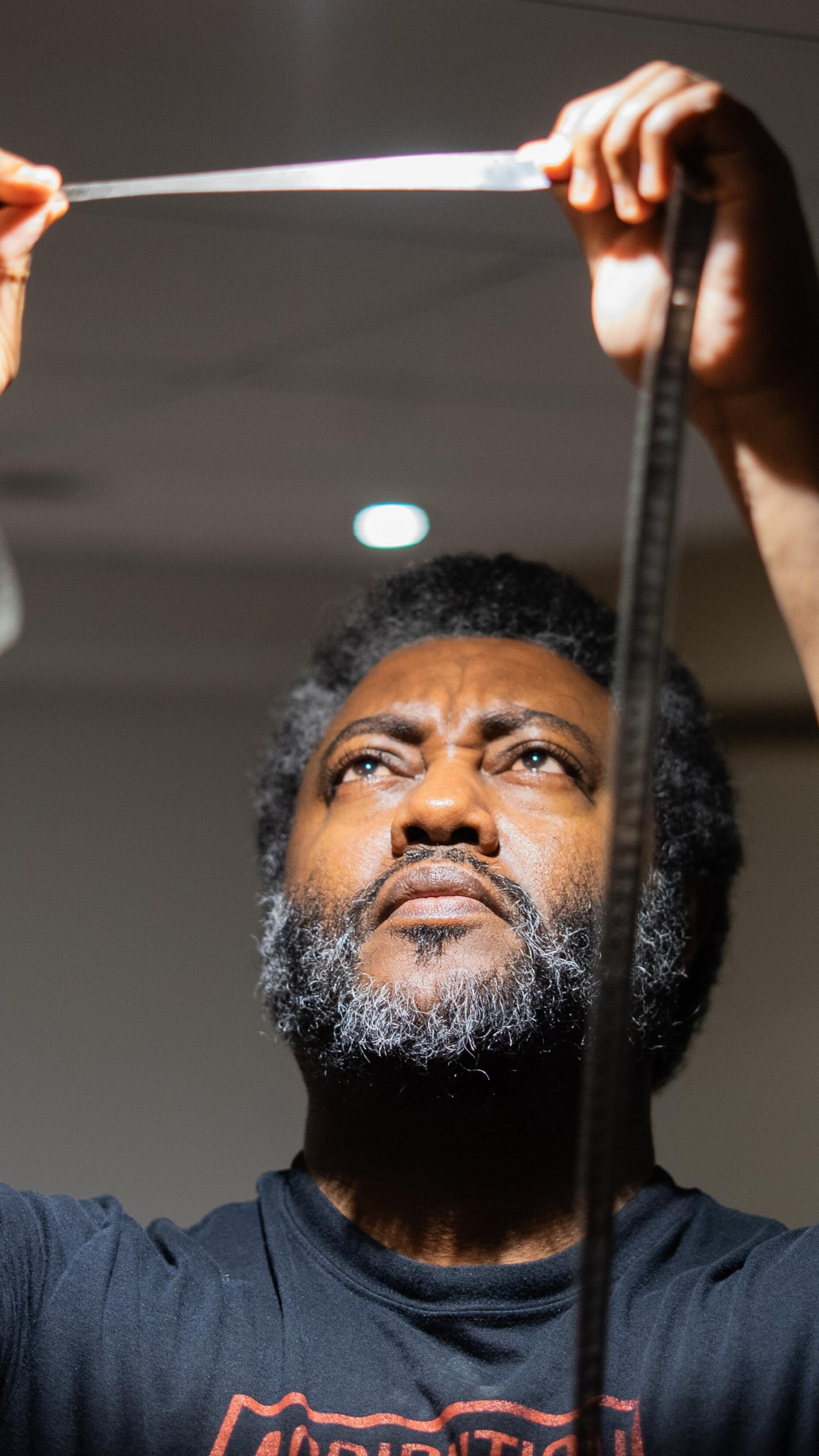Elyas Tesfaye examine une pellicule tenue entre ses deux mains sous la lumière de son plafonnier, à Winnipeg, en juillet 2026.