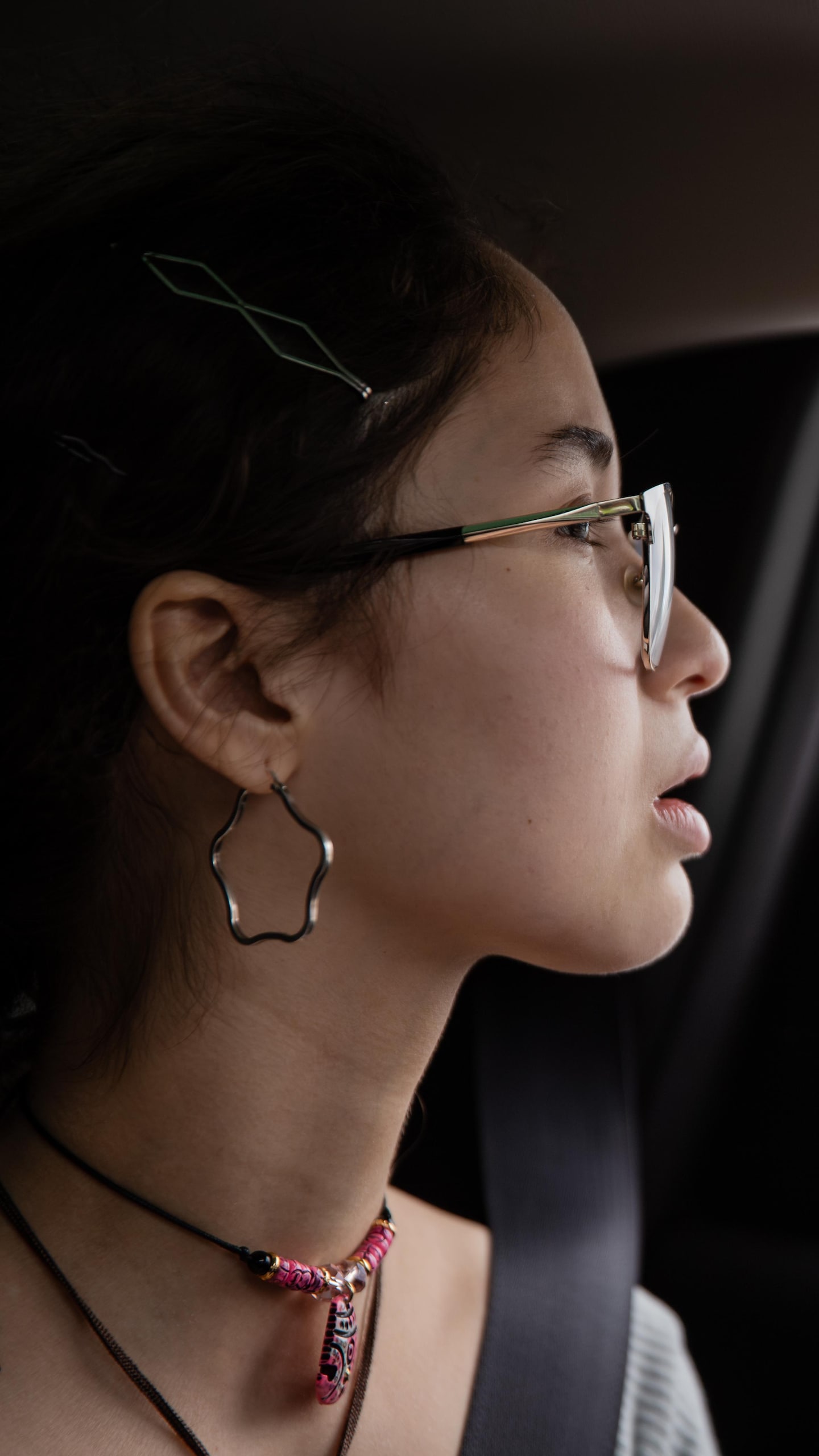 Gros plan de profil d'une jeune femme à lunettes dans un véhicule, observant l'extérieur par la fenêtre ouverte.