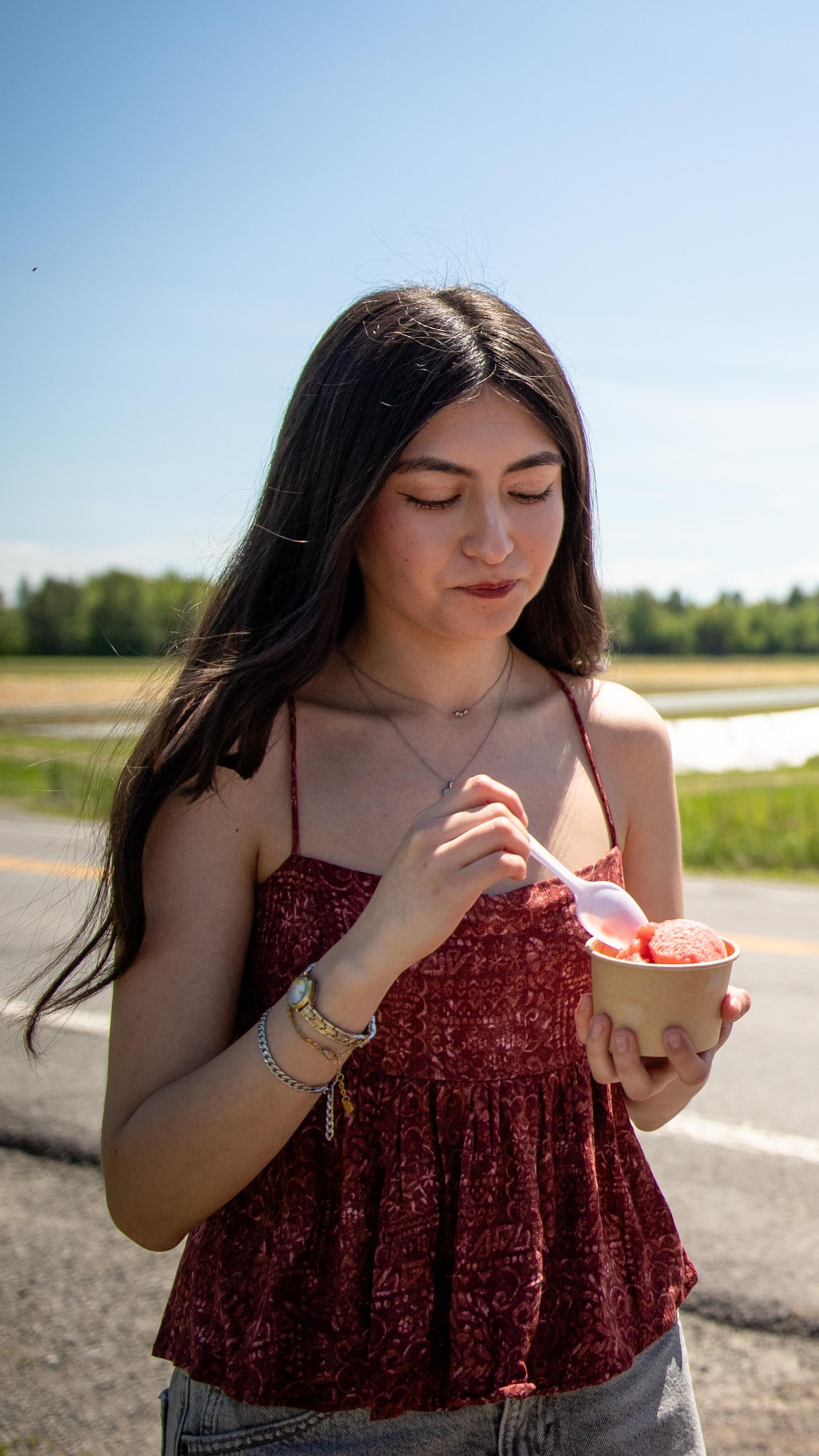 Deux jeunes femmes mangent de la crème glacée au bord d'une route longeant des champs.