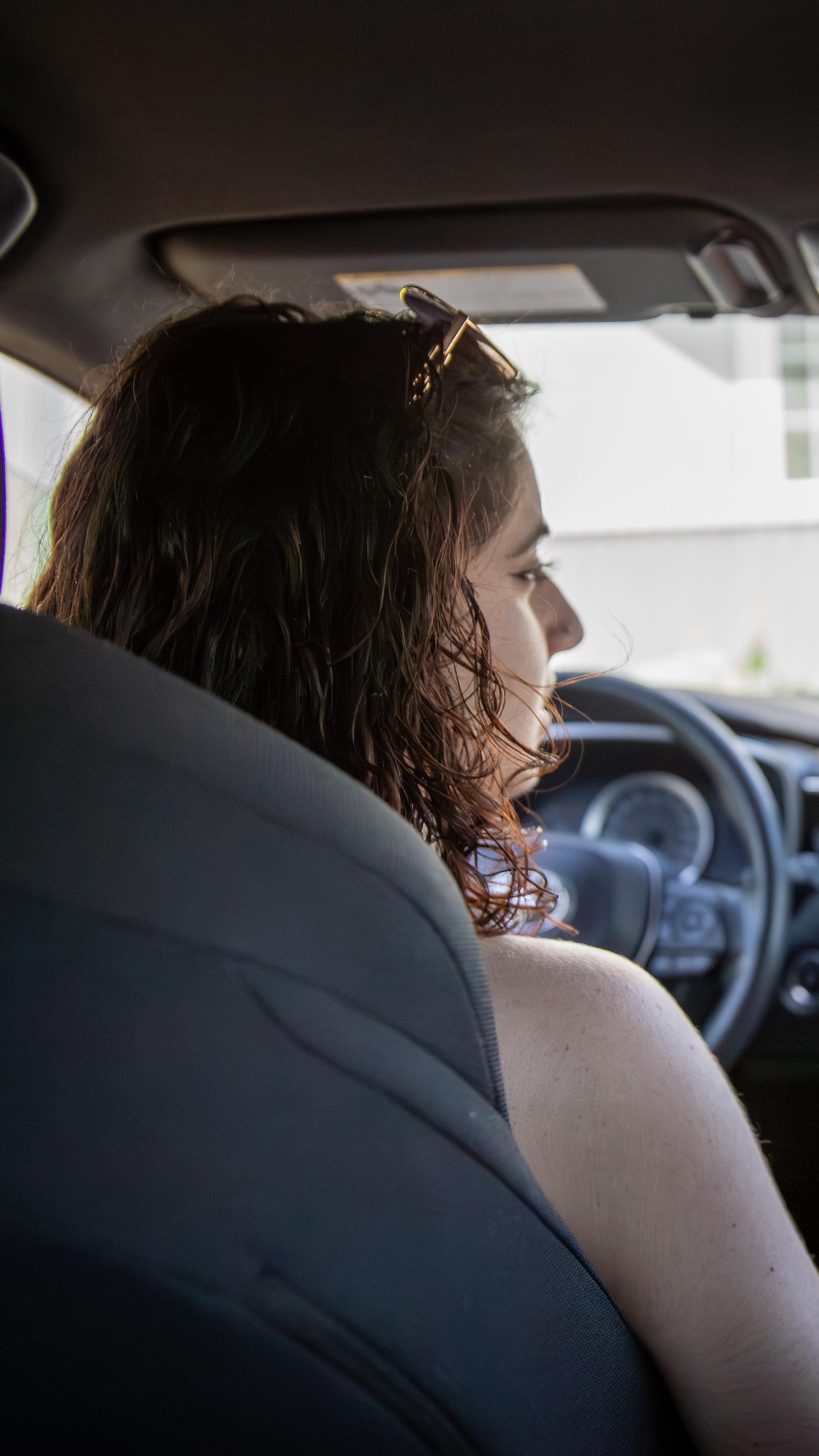 Depuis le siège arrière d'une voiture, on voit deux femmes assises à l'avant. Une guirlande de fleurs est suspendue au rétroviseur.