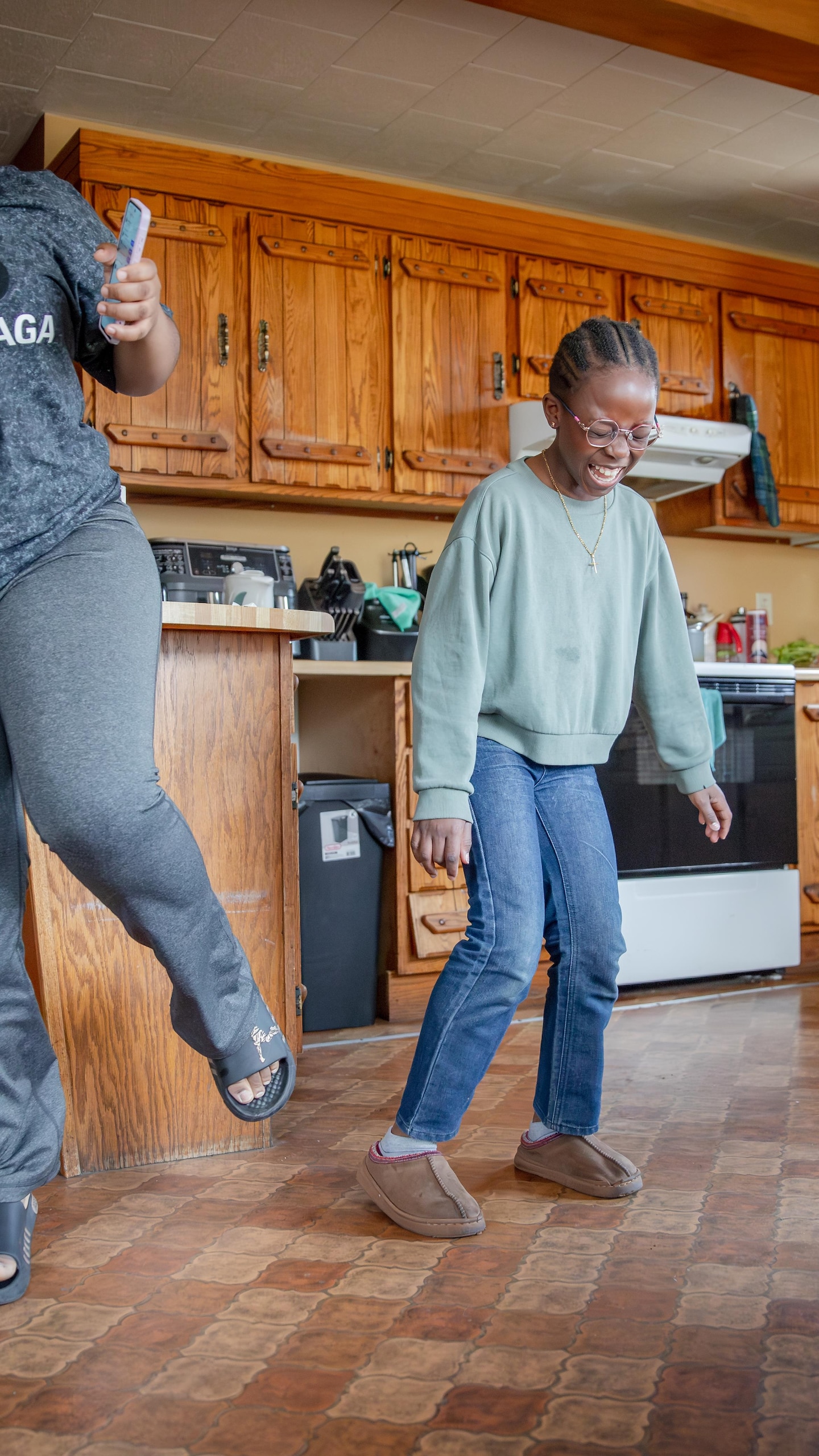 Une jeune femme et une fillette rient et dansent ensemble sur le plancher en linoléum de leur cuisine.
