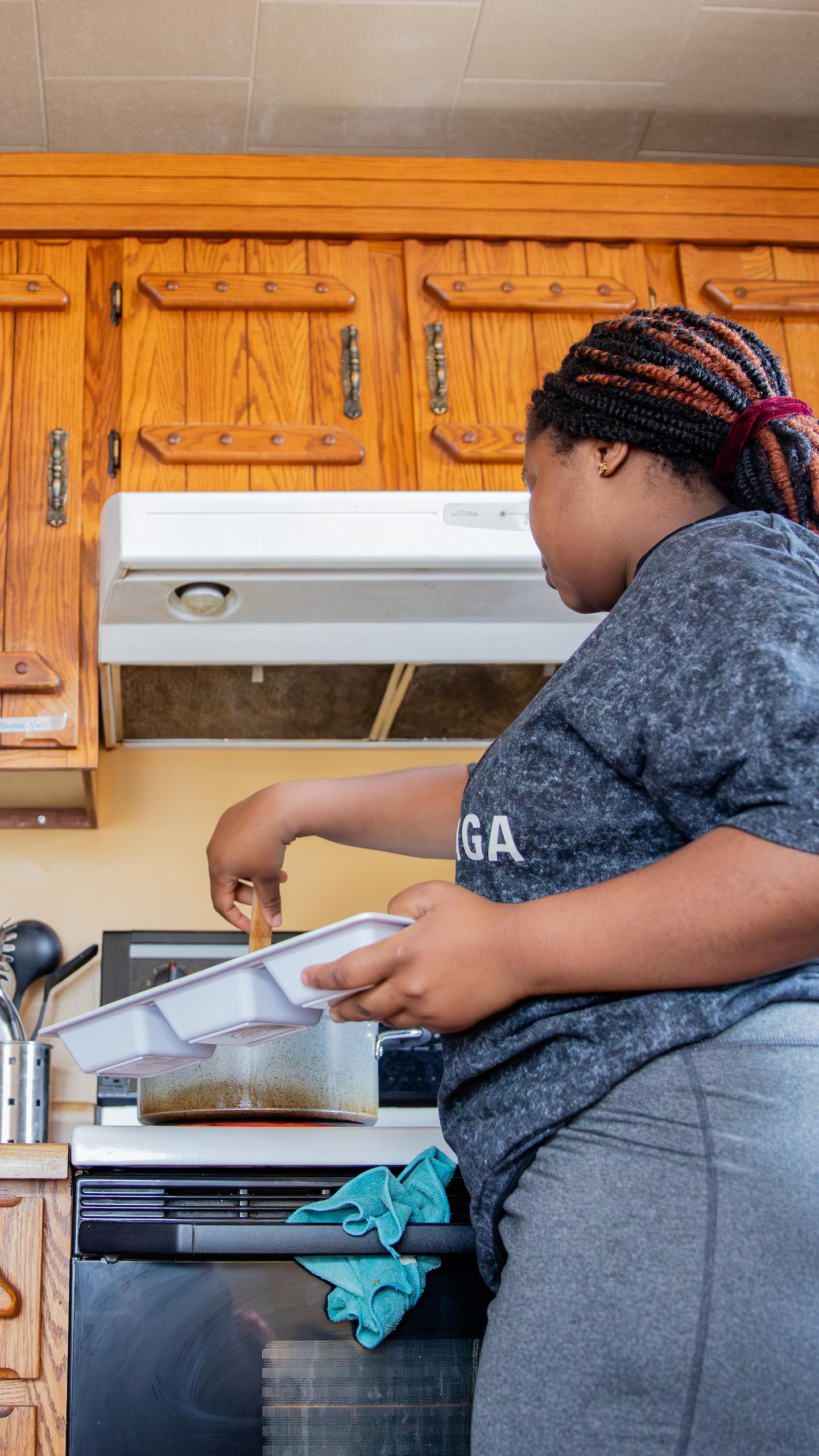 Une jeune femme cuisine dans un chaudron sur une cuisinière pendant qu'une fillette l'observe.