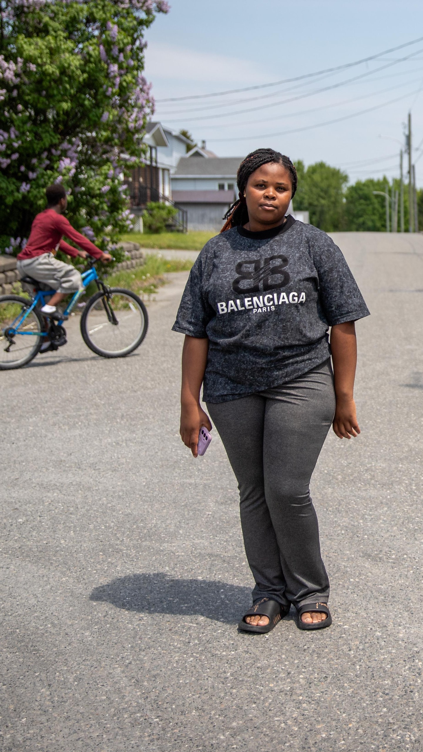 Une jeune femme debout dans le milieu d'une rue, avec un jeune homme à bicyclette à l'arrière.