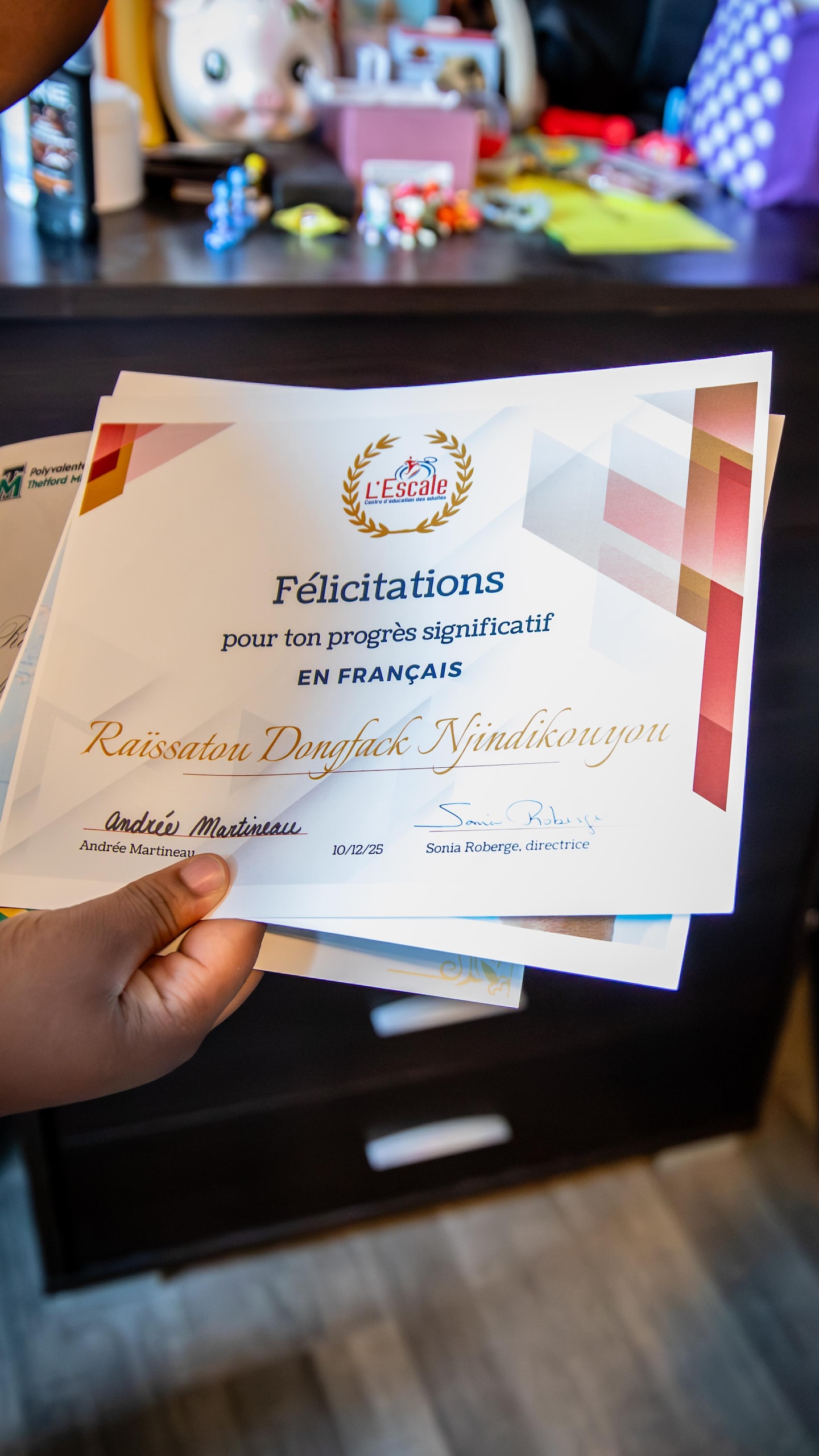 Une personne tient un certificat de félicitations pour ses progrès significatifs en français au nom de Raissatou Dongfack Njindikouyou.