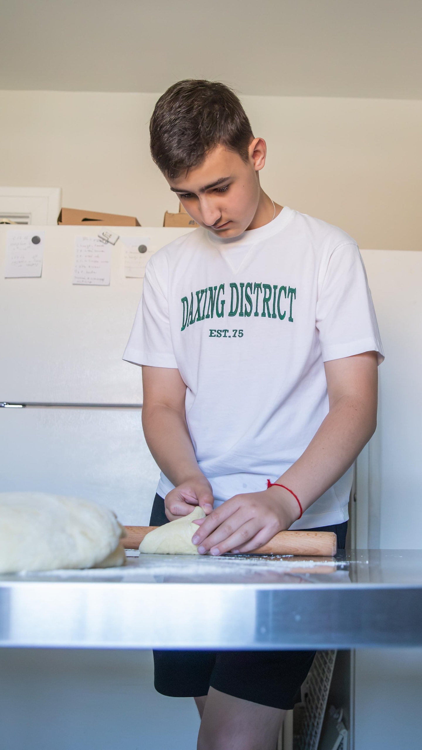 Un jeune homme abaisse de la pâte avec un rouleau à pâtisserie sur une table de travail dans une cuisine.