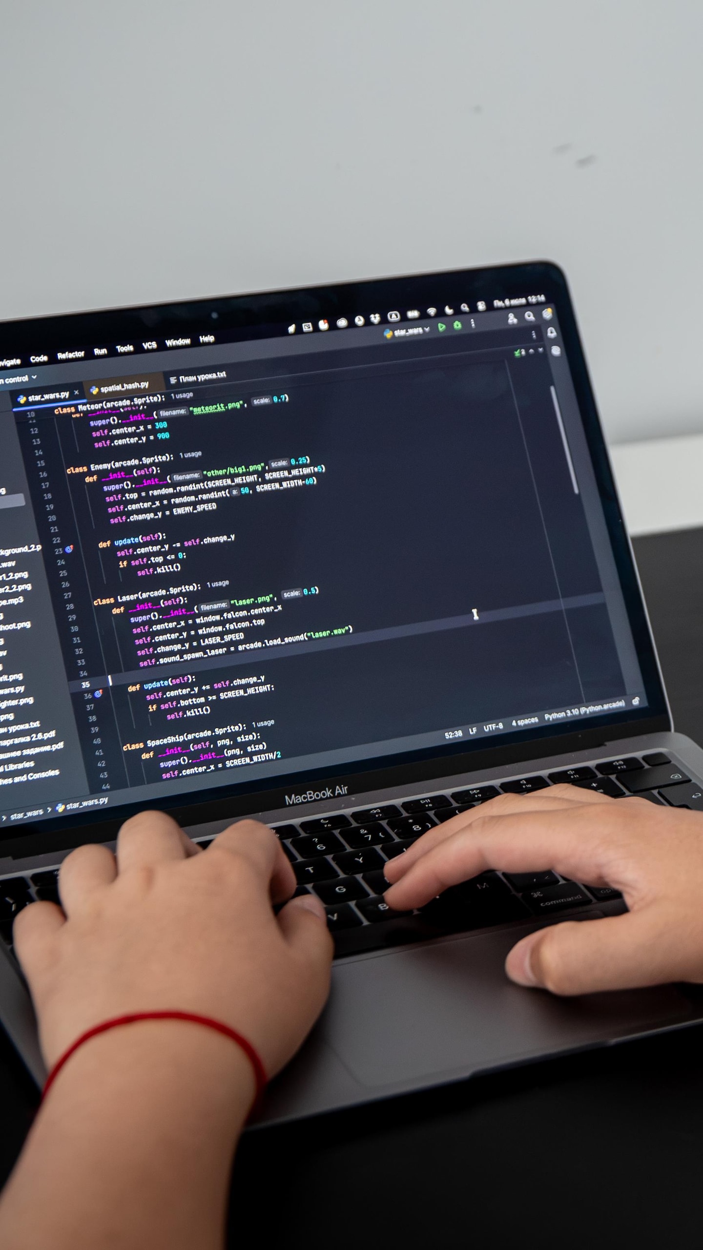 Un jeune homme, vu de dos par-dessus l'épaule, tape du code informatique sur un ordinateur portable posé sur un bureau.