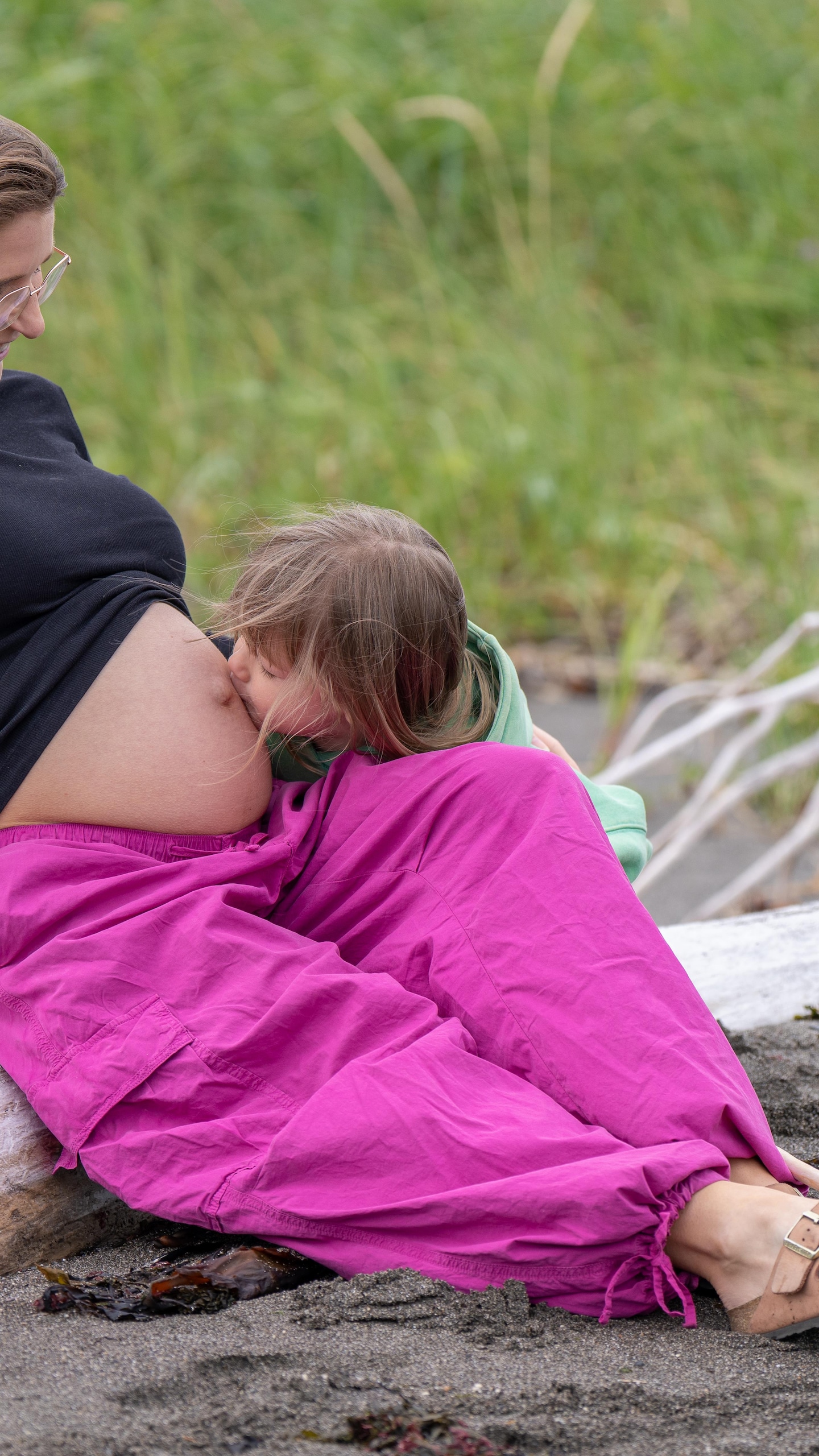 Une femme enceinte est assise sur la plage avec son fils de 4 ans. Ce dernier donne un bisou sur le ventre arrondi de sa maman.