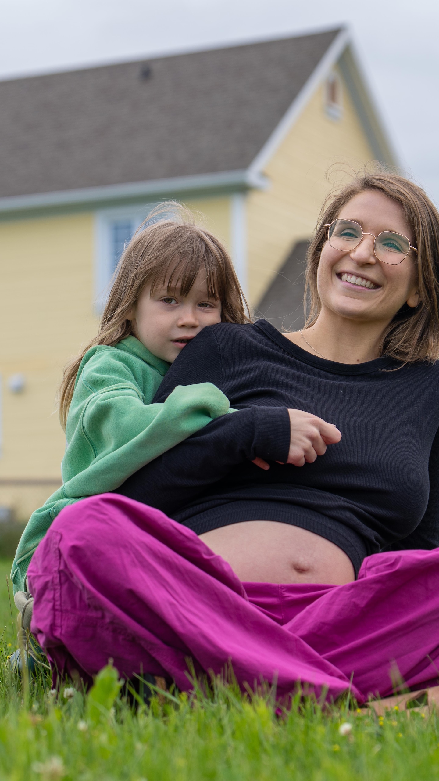 Une femme enceinte est assise sur le gazon, derrière sa maison. Son fils de 4 ans l'enlace, la tête appuyée sur son épaule.