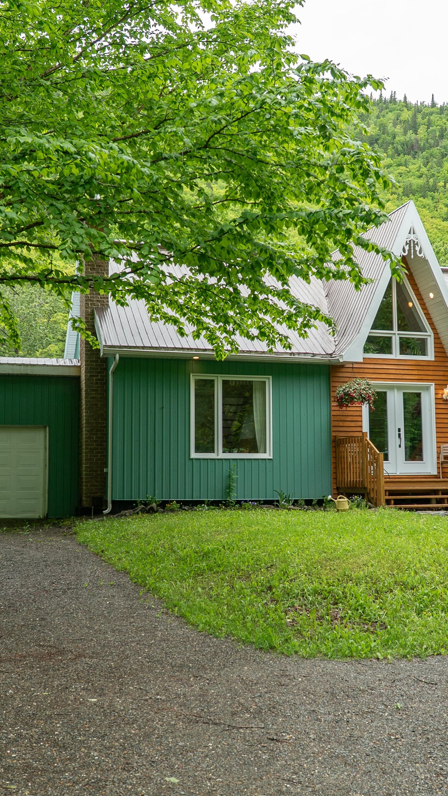Une voiture est stationnée devant une jolie maison verte, entourée d'arbres et de montagnes.