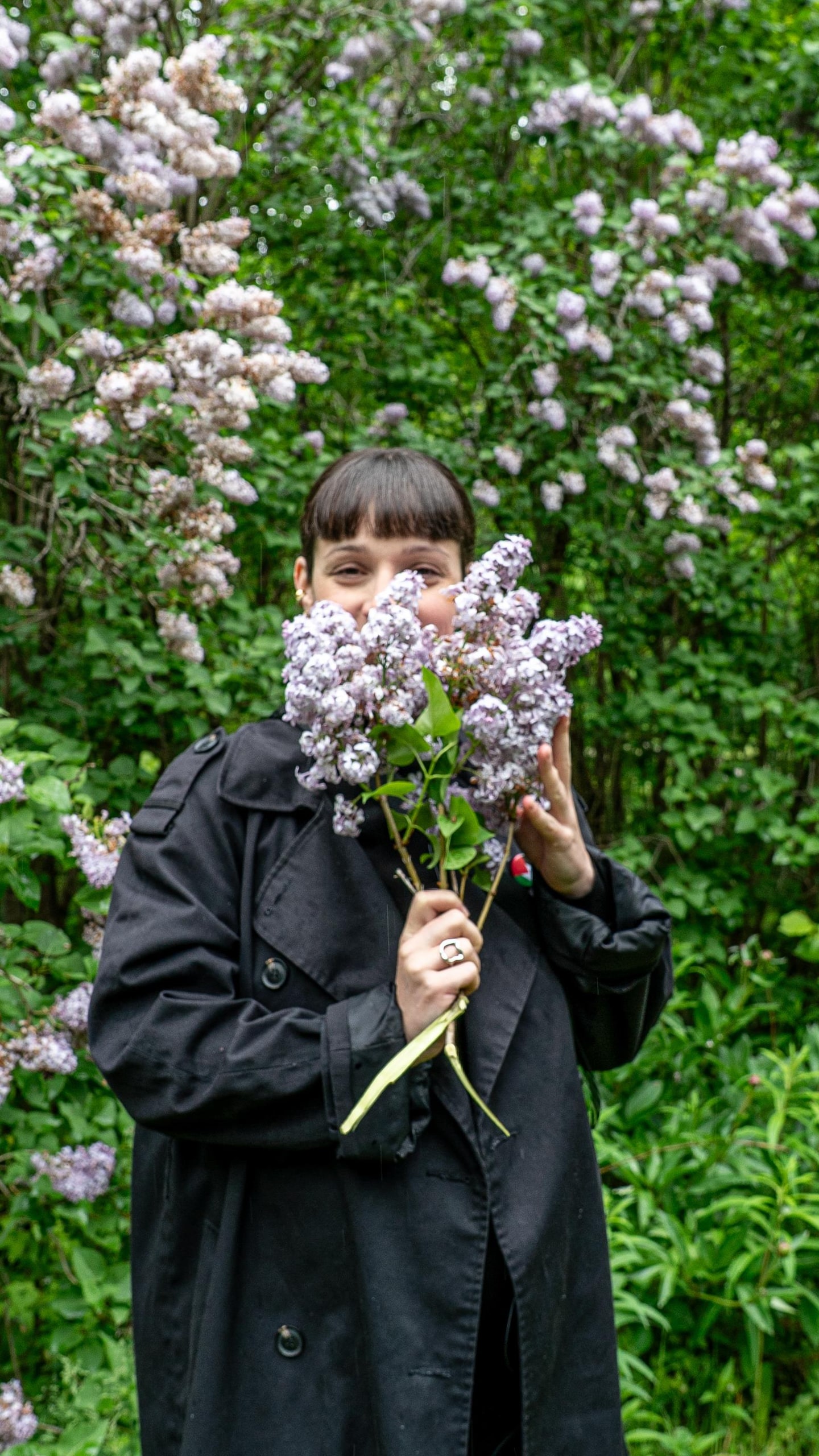 Priscilla sourit en tenant un bouquet de lilas devant son visage.
