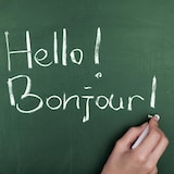 Une femme écrit « Hello! Bonjour ! » sur un tableau vert.


