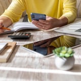 Une personne planifie ses finances avec son téléphone intelligent en main, un cahier, une calculatrice, un ordinateur portable et une tablette.