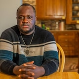 Une personne assise à une table, les mains entrelacées.