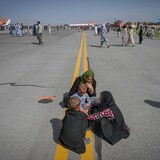 Afghan people sit along the tarmac as they wait to leave the Kabul airport.