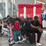 Travellers sitting on and around their luggage in an airport departure hall.