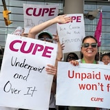 Demonstrators at an airport holding signs saying 'Underpaid and Over It' and 'Unpaid work won't fly'.