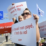 Des agents de bord d'Air Canada qui débrayent dehors à l'aéroport international Montréal-Trudeau tiennent des affiches de leur syndicat avec le message « Le travail non payé, c'est du vol ».