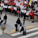 Travellers walking by protesters holding signs at an airport.