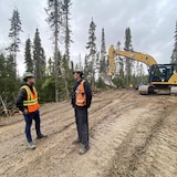 Alexandre Girard discute avec le superviseur d'un chantier dans la forêt près d'une pelle mécanique qui aménage un chemin.