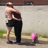 A woman holds her teenage daughter in her arms, with the flowers they brought at their feet.