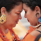 Deux femmes habillées en orange se tiennent front contre front, les yeux fermés.