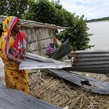 Des femmes sur le bord d'une rivière transportent des plaques de métal rouillées.