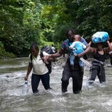 Haitian migrants wade through a river as they cross the Darien Gap, from Colombia into Panama, hoping to reach the U.S. on Oct. 15, 2022. One expert says the number of migrants making the perilous crossing suggests this summer will break all previous records for irregular migration into North America. (Fernando Vergara/Associated Press)