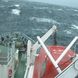 The bow of a boat is shown against stormy waters. 