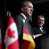 Deux hommes parlant devant les drapeaux de l'Allemagne et du Canada.
